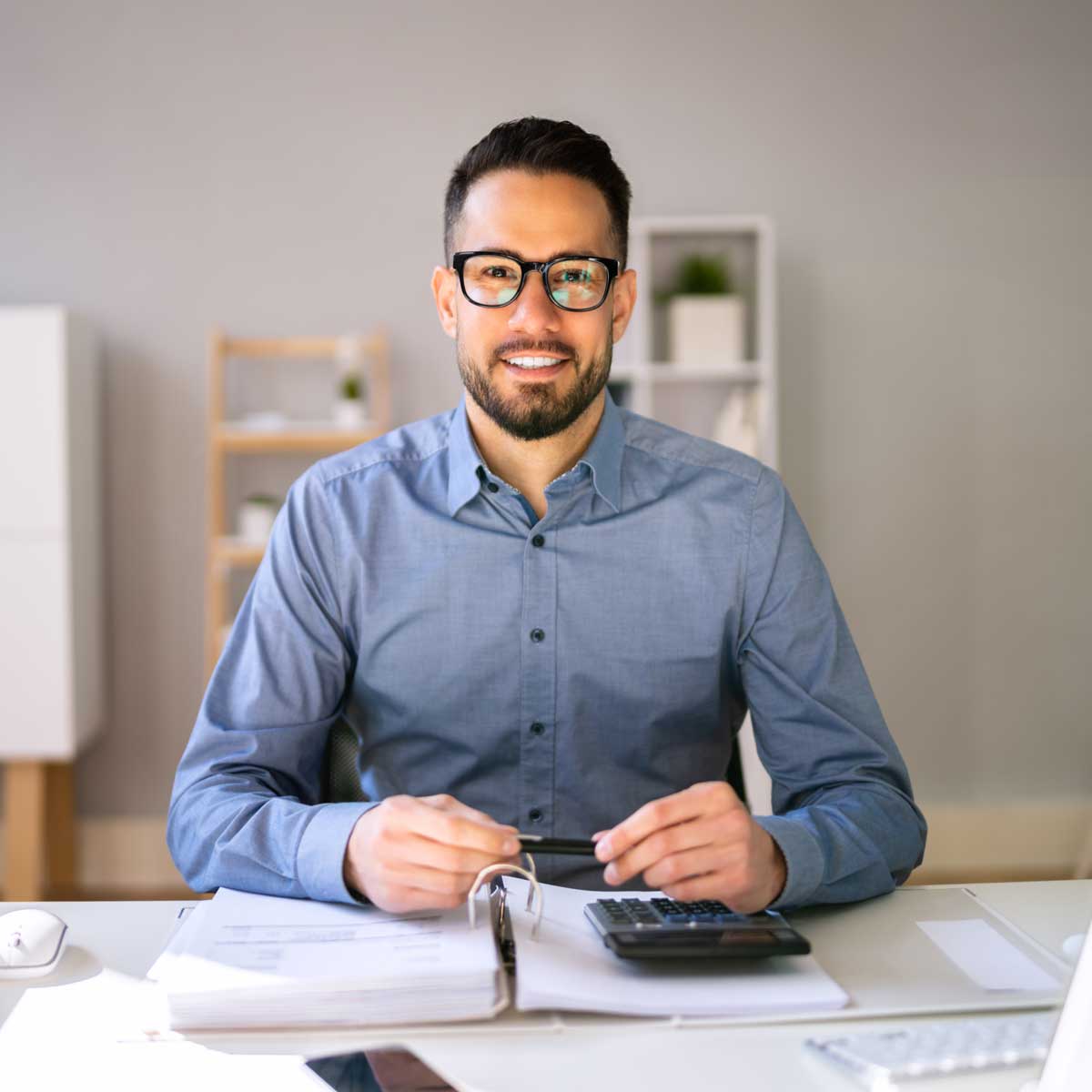Ein Mann sitzt am Schreibtisch und grinst in die Kamera