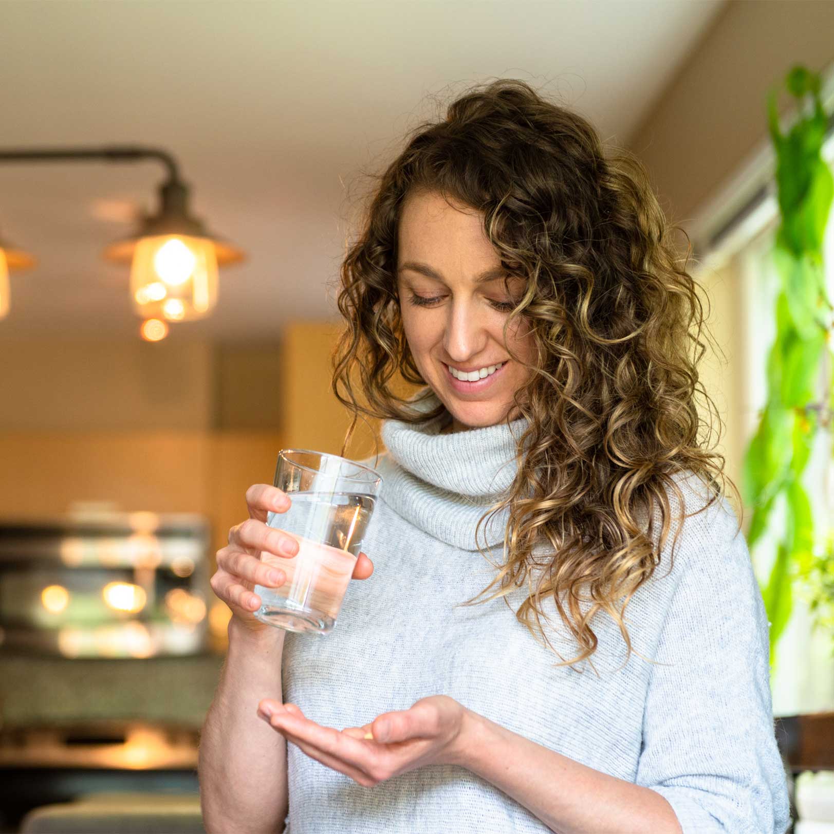 Lachende Frau hält Tabletten und ein Glas Wasser in der Hand