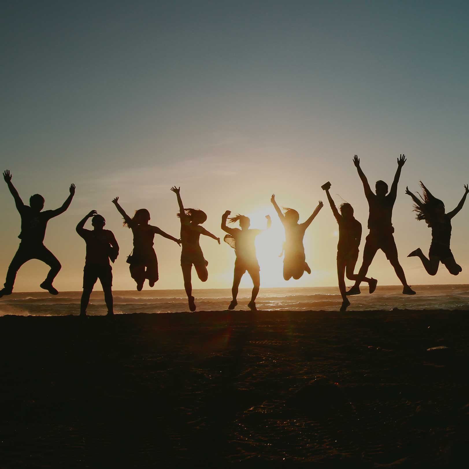 Gruppe Menschen die im Sonnenuntergang in die Luft springt 