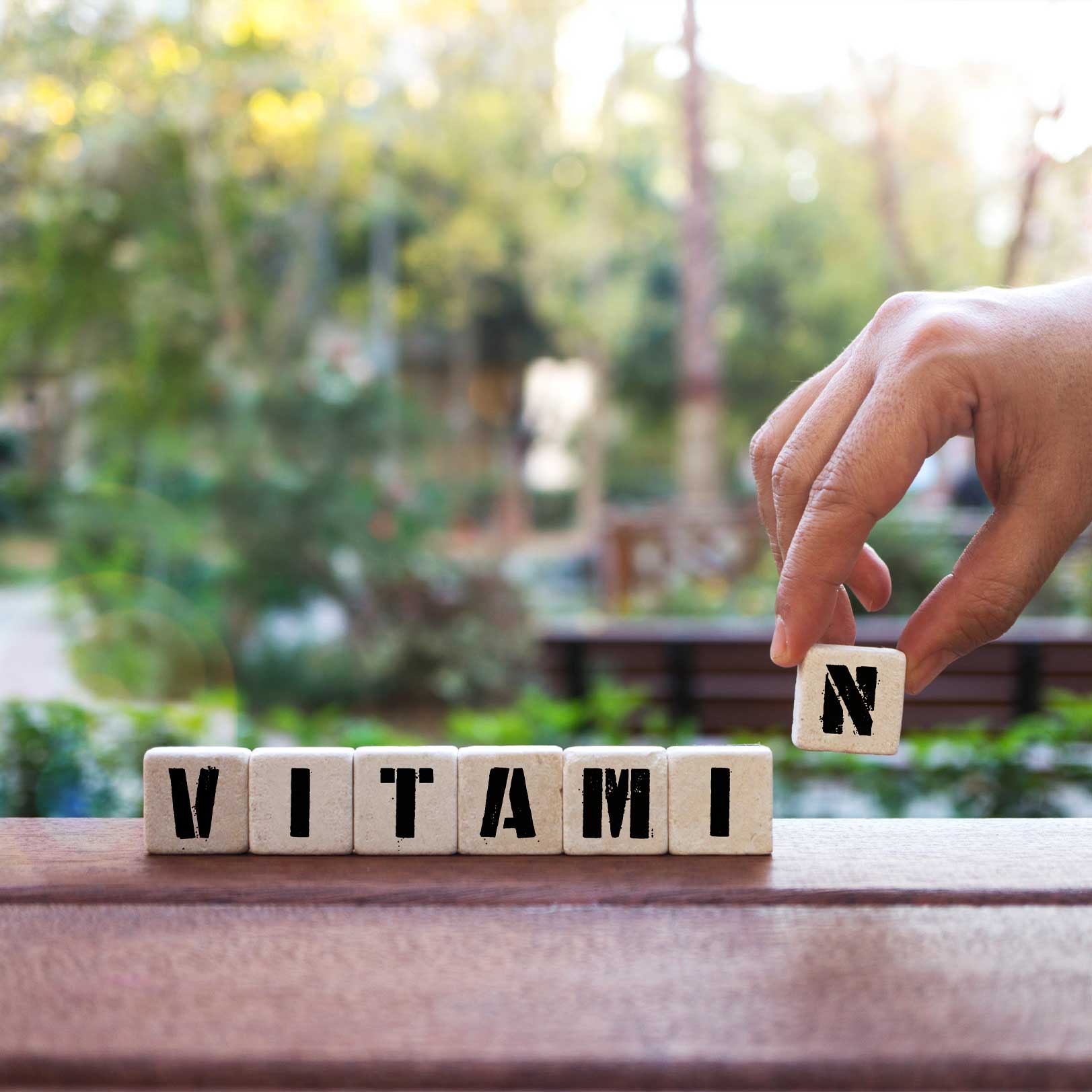 Eine Hand packt Würfel mit Buchstaben auf eine bank auf denen steht Vitamin